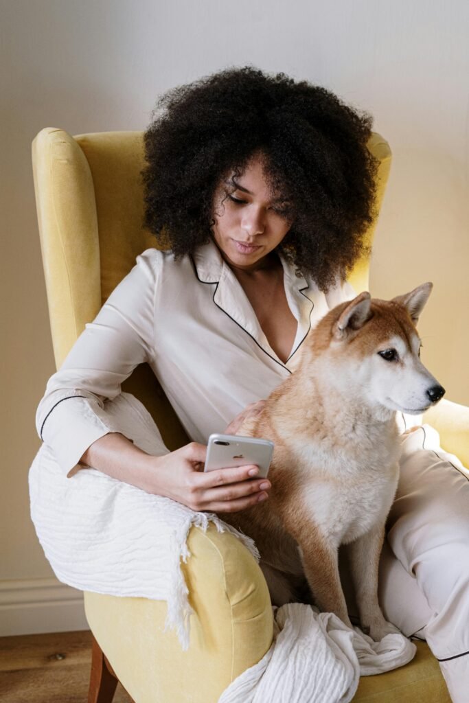 pexels photo 4056509 4056509 Woman with afro hair sitting in an armchair at home, holding a smartphone and petting her Shiba Inu dog.